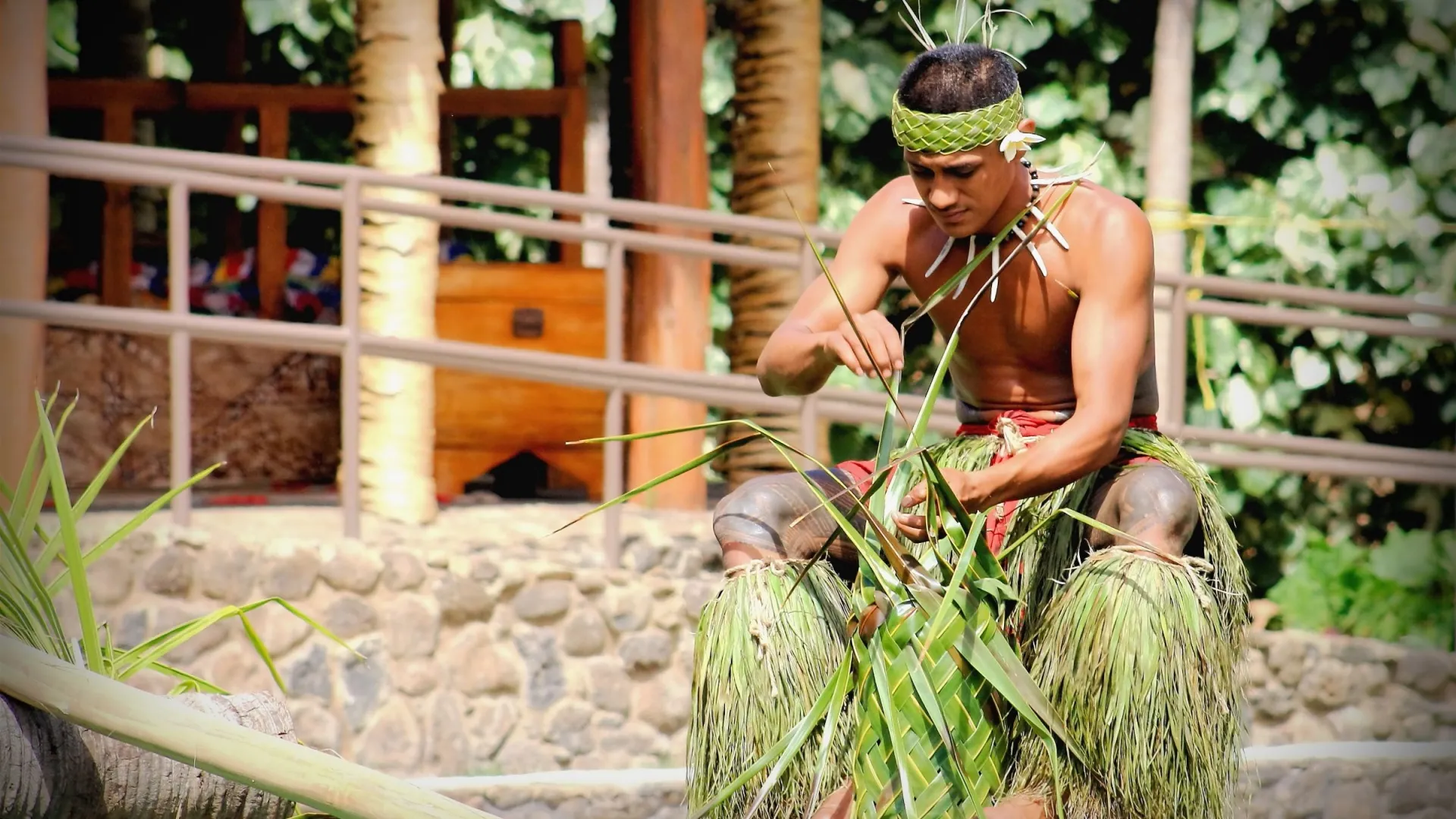 Man weaving palm leaves, wearing traditional attire, outdoors.